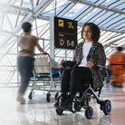 Frau im faltbaren Elektrorollstuhl am Flughafen auf dem Weg zum Gate
